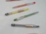 Plusieurs stylos de différentes couleurs sont alignés sur une surface blanche.