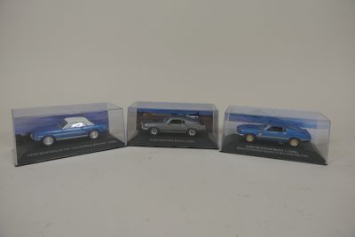 trois petites voitures sont posées dans une vitrine, sur une surface blanche