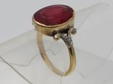 une image représentant une bague ornée d'une pierre rouge posée sur un morceau de verre transparent