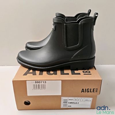 des bottes en caoutchouc noires posées sur une boîte, sur une surface blanche