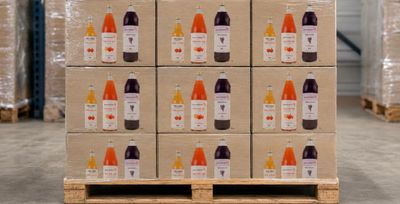 Des cartons de jus de fruits sont posés sur des palettes dans un entrepôt, avec d'autres palettes en arrière-plan