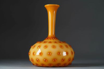 un vase orange posé sur une table blanche, près d'un mur gris