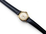 un gros plan d'une montre avec un bracelet noir posée sur une surface blanche