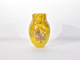 un vase jaune orné de fleurs, posé sur une surface blanche