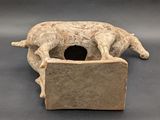 sculpture of a dog resting on a block with a hole in it