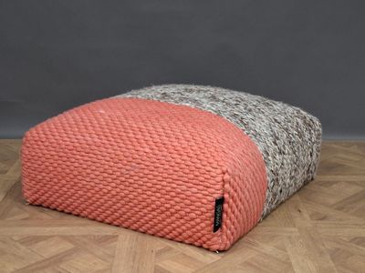 a pink and grey knitted pouft sitting on a wooden floor