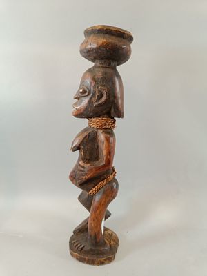 une image représentant une statue en bois d'un homme portant un bol sur la tête