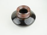 a black vase with a brown lid on a white surface