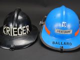 pair of fire helmets with nameplates on them sitting on a black surface