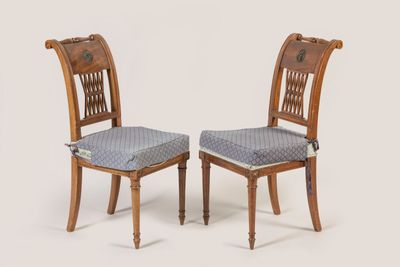 two wooden chairs with patterned seat pads on them against a white background