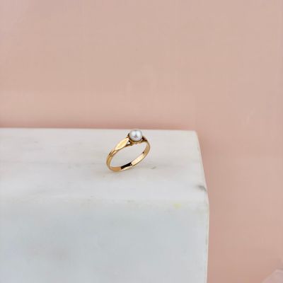 un gros plan d'une bague en or ornée d'une perle, posée sur un bloc de marbre