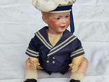 a small doll of a sailor sitting on a white sheet