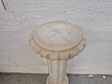 a white bird bath sitting on the ground next to a white wall