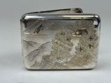 a silver cigarette case with a picture of a mountain scene on it