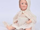 a doll that is sitting on the ground wearing a white dress and bonnet