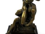bronze statue of a woman sitting on a rock with a hat on her head