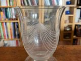 un vase en verre posé sur une table devant une bibliothèque