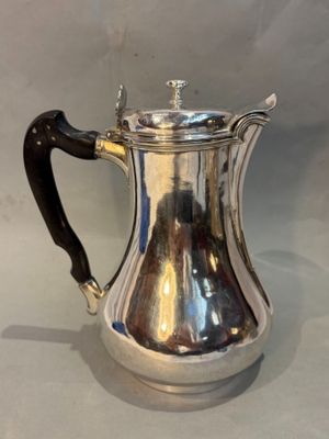 silver plated coffee pot with black handle on white background