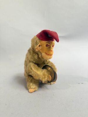 un petit singe en peluche coiffé d'un bonnet rouge, assis sur un tonneau