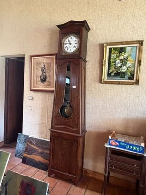 une horloge de parquet au milieu d'une pièce, avec des tableaux accrochés aux murs
