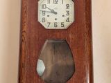 une horloge en bois accrochée au mur à côté d'un vase