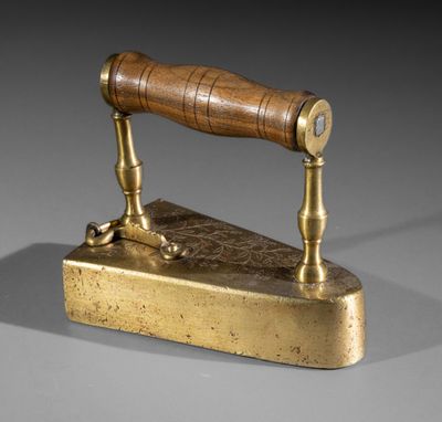 an antique brass iron with a wooden handle on a gray surface