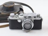 a black and white photo of a camera and a brown bag