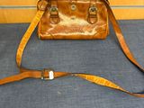 un sac à main en cuir posé par terre, avec une sangle autour