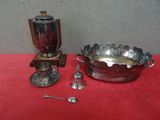 un bol en argent avec des cuillères et un repose-cuillères posé sur une table rouge