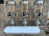 three drinks dispensers sitting on a table in front of a stone wall
