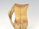 a wooden pitcher with a curved handle on a white surface