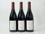 trois bouteilles de vin rouge sont alignées sur une surface blanche