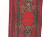 an old book with a red cover sitting on top of a table
