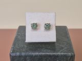 une paire de boucles d'oreilles en émeraude exposées sur un bloc de marbre