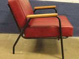 a red chair with a wooden arm rest on a concrete floor