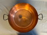 a large copper pan with a handle on a table