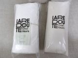 two bags of white towels sitting next to each other on top of a table
