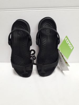 une paire de sandales noires posées sur une surface blanche, avec une étiquette de prix