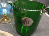 a green glass pitcher sitting on a table next to a blue glass