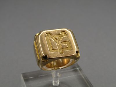 a close up of a gold signet ring on a clear stand