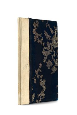 an old book with a black cover sitting on a white surface