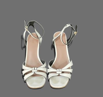 a pair of women ' s white sandals with a bow on the heel