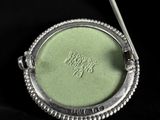 a silver spoon sitting in front of a green eye shadow