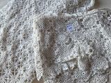 une veste blanche au crochet posée sur un lit, à côté d'un oreiller