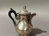 an antique silver coffee pot with a black handle on a table