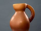 brown vase sitting on top of a white pedestal against a gray wall