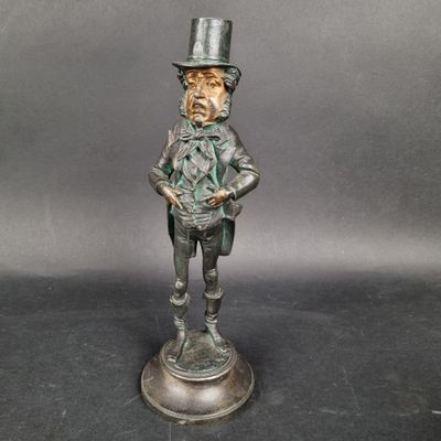 une vieille statue en bronze représentant un homme coiffé d'un haut-de-forme et muni d'une canne