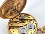a gold pocket watch with gears inside of it on a white surface