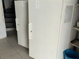 two white refrigerators in a room with a blue bucket on the floor