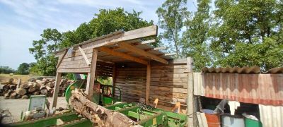 a tractor parked in front of a shed with a pile of wood